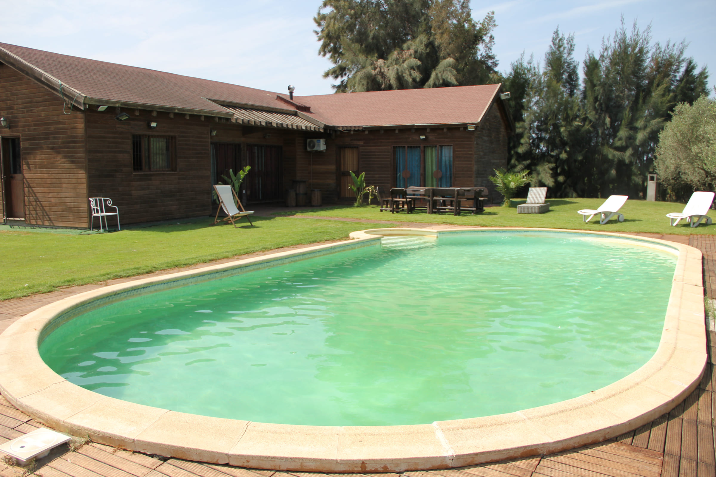 Piscine ovale du Chalet Essanya bordée de pelouse, devant le chalet en bois